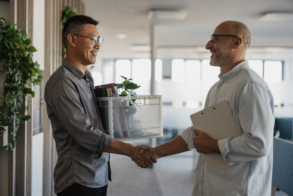 Two professionals shake hands in a modern office space following a reduction in force process.